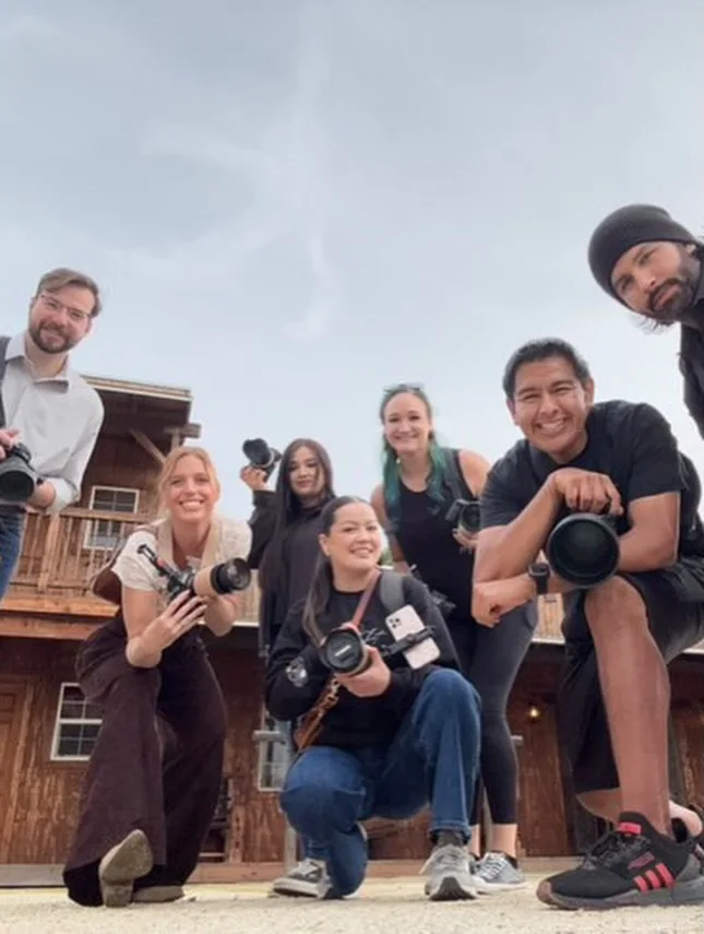 Group of photographers posing together with cameras at a rustic location.